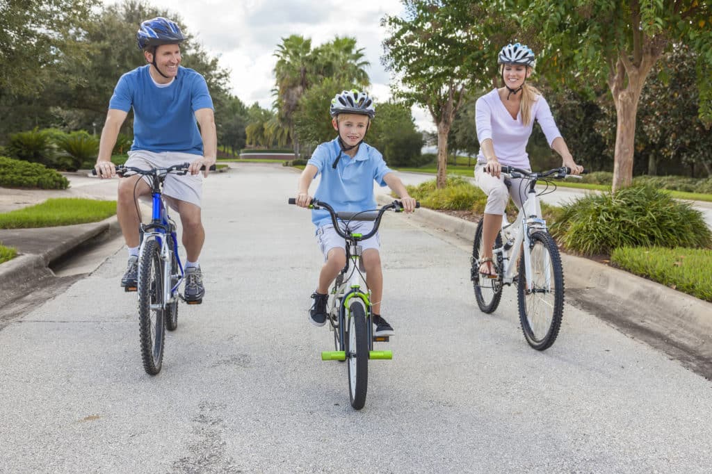 Parents and their young son riding bikes together on a neighborhood street
